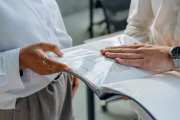 Hände eines Mitarbeiters halten Kündigungsschreiben und Sozialplan-Dokumente vor neutralem Hintergrund
